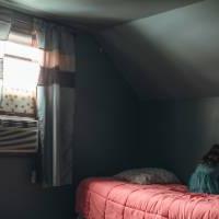 Little girl sitting on red bed with head against wall in darkened room